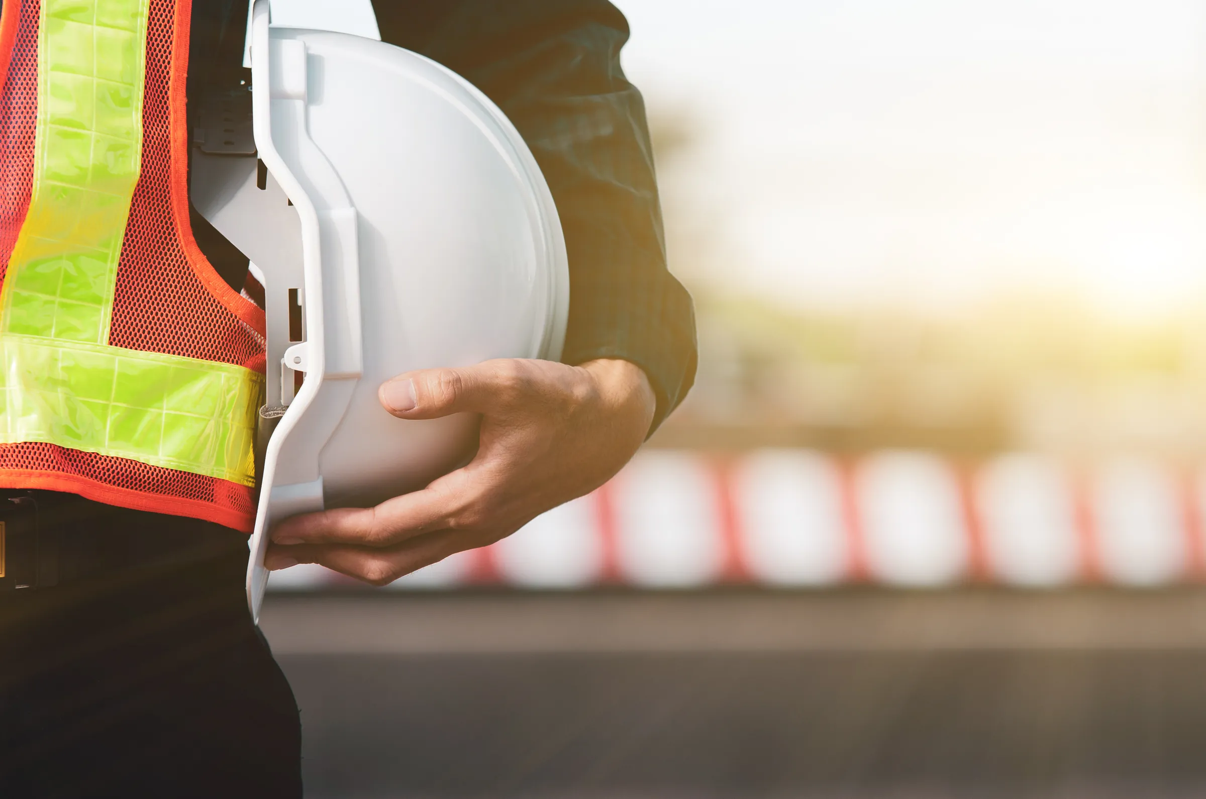 Construction worker holding a hard hat beside high-visibility safety clothing.