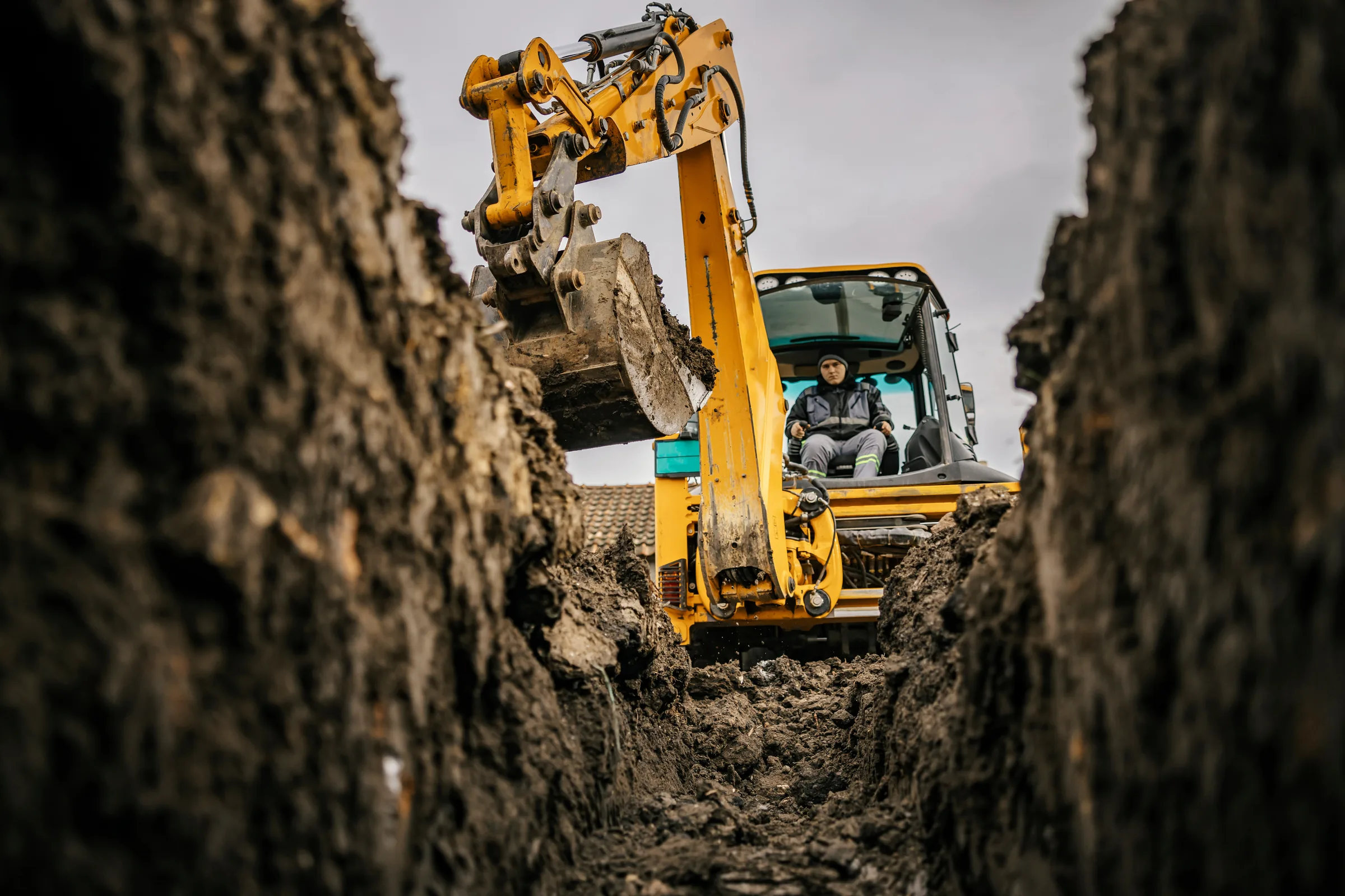 Construction plant operator using an excavator from within a trench.
